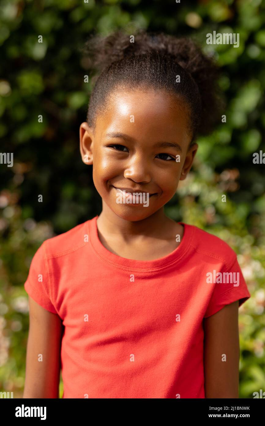 Portrait of cute smiling african american girl standing against plants ...
