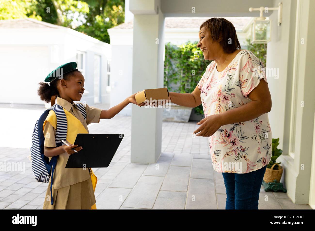 Smiling african american scout girl in uniform delivering package to senior woman at home Stock Photo
