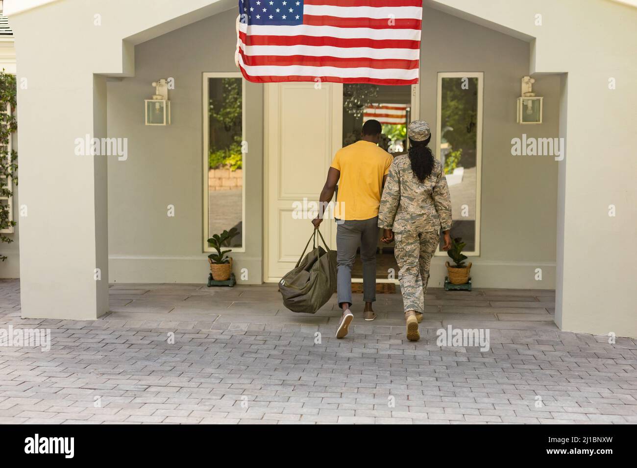 Portrait of happy female mid adult african american soldier entering home with husband Stock Photo