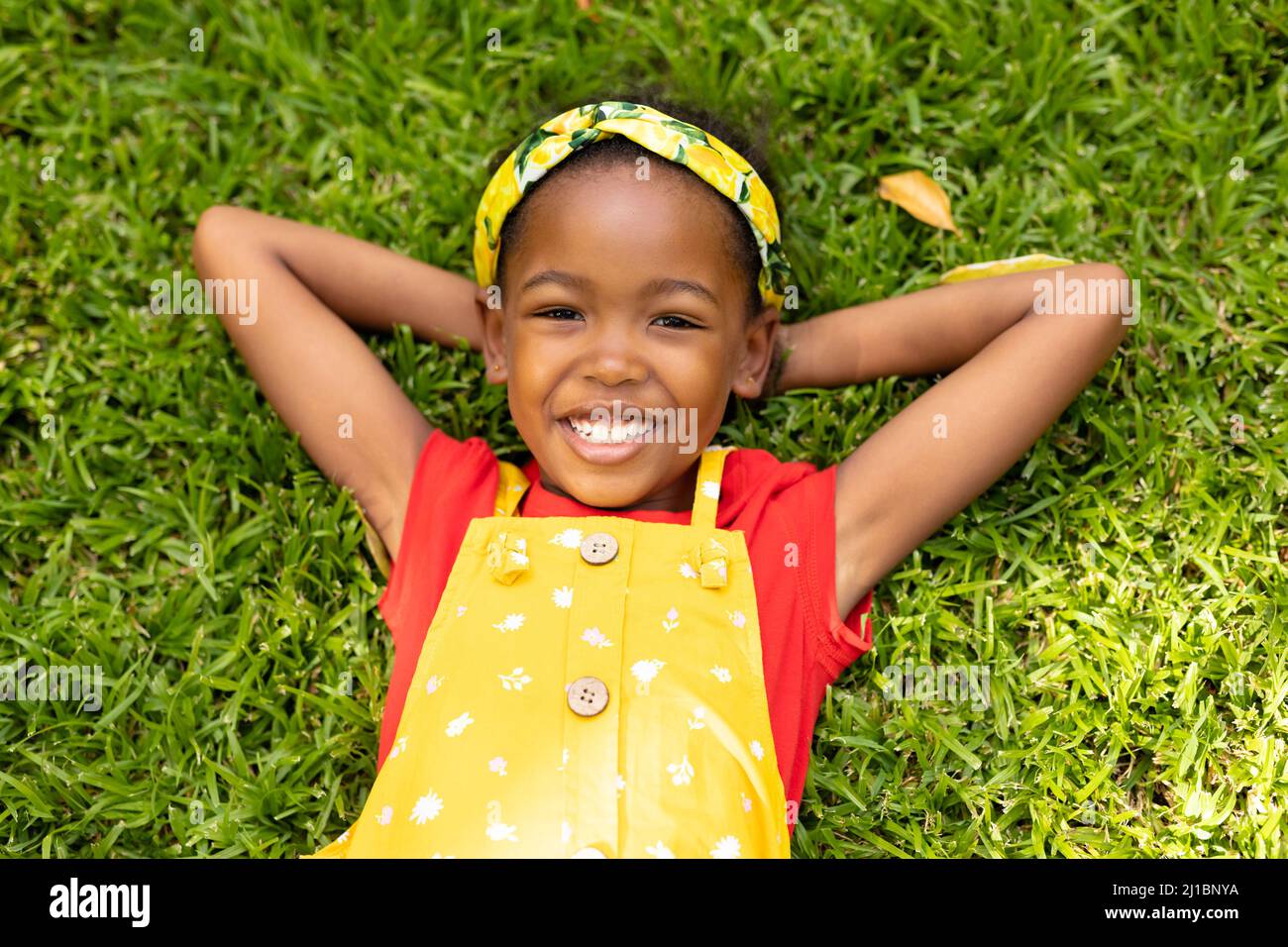 High angle portrait of smiling african american girl lying with hands behind head in backyard Stock Photo
