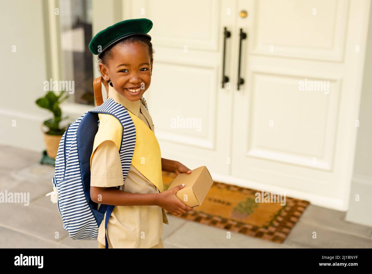 Smiling african american scout girl in uniform delivering package at home Stock Photo