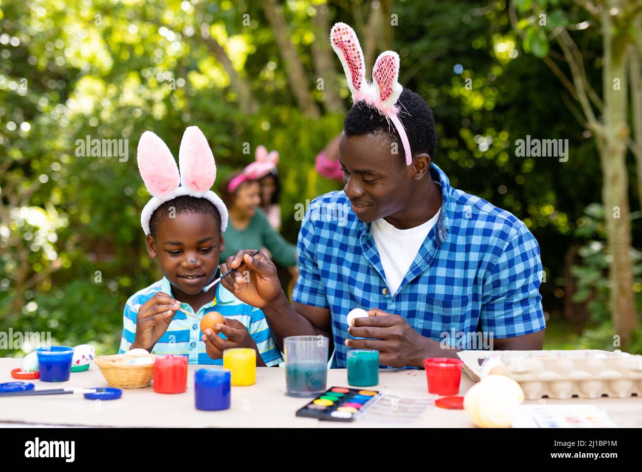 African american boy and father painting easter eggs while family in background Stock Photo