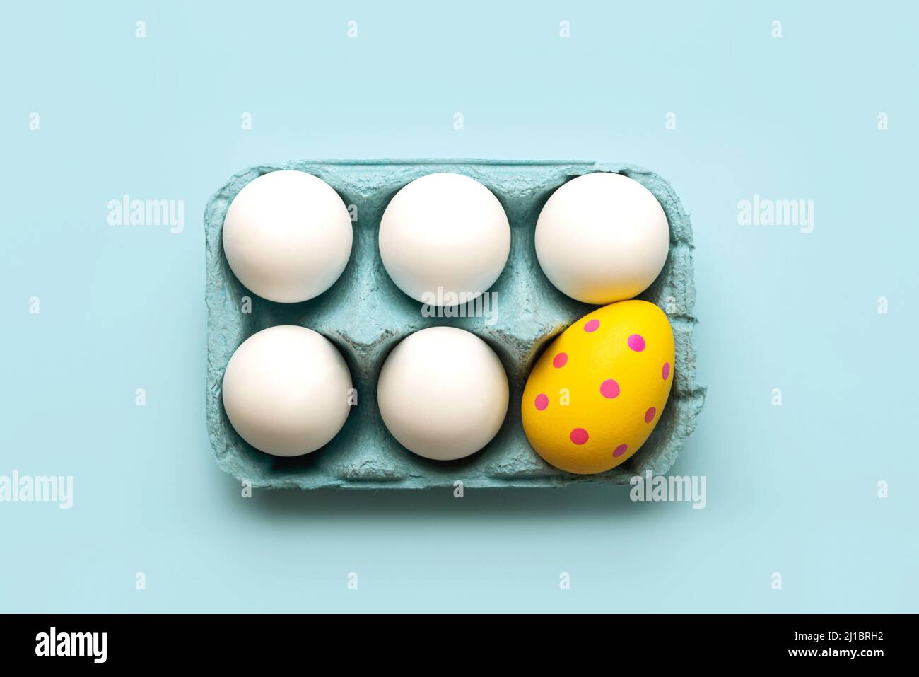 Happy Easter. Top view of chicken eggs and easter painted egg in an open blue cardboard box over blue background Stock Photo