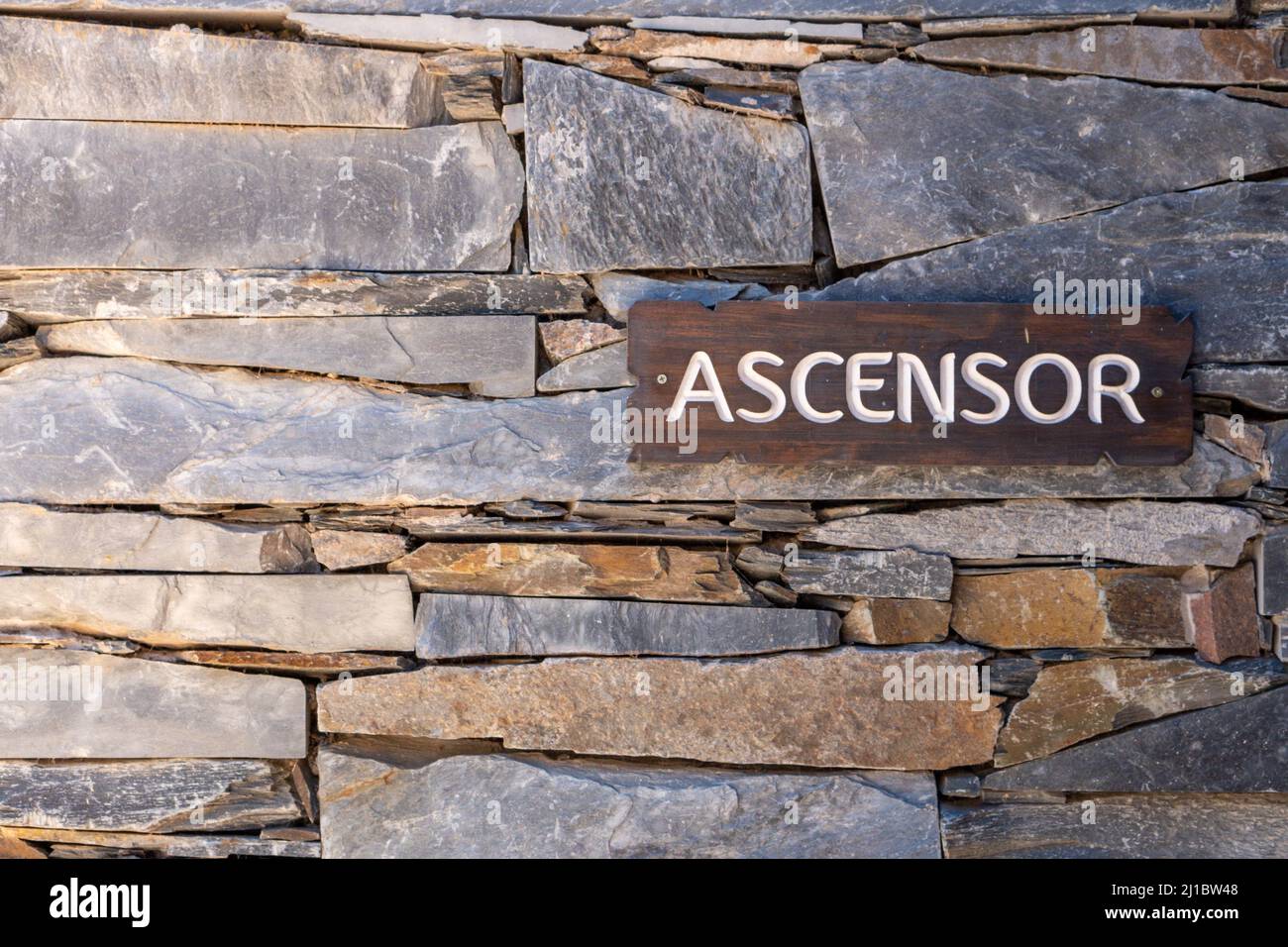 A closeup of a stone wall with a wooden sign saying "ascensor" which
