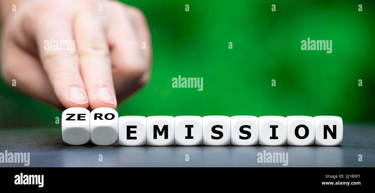 Hand turns dice and changes the expression 'emission' to 'zero emission'. Stock Photo