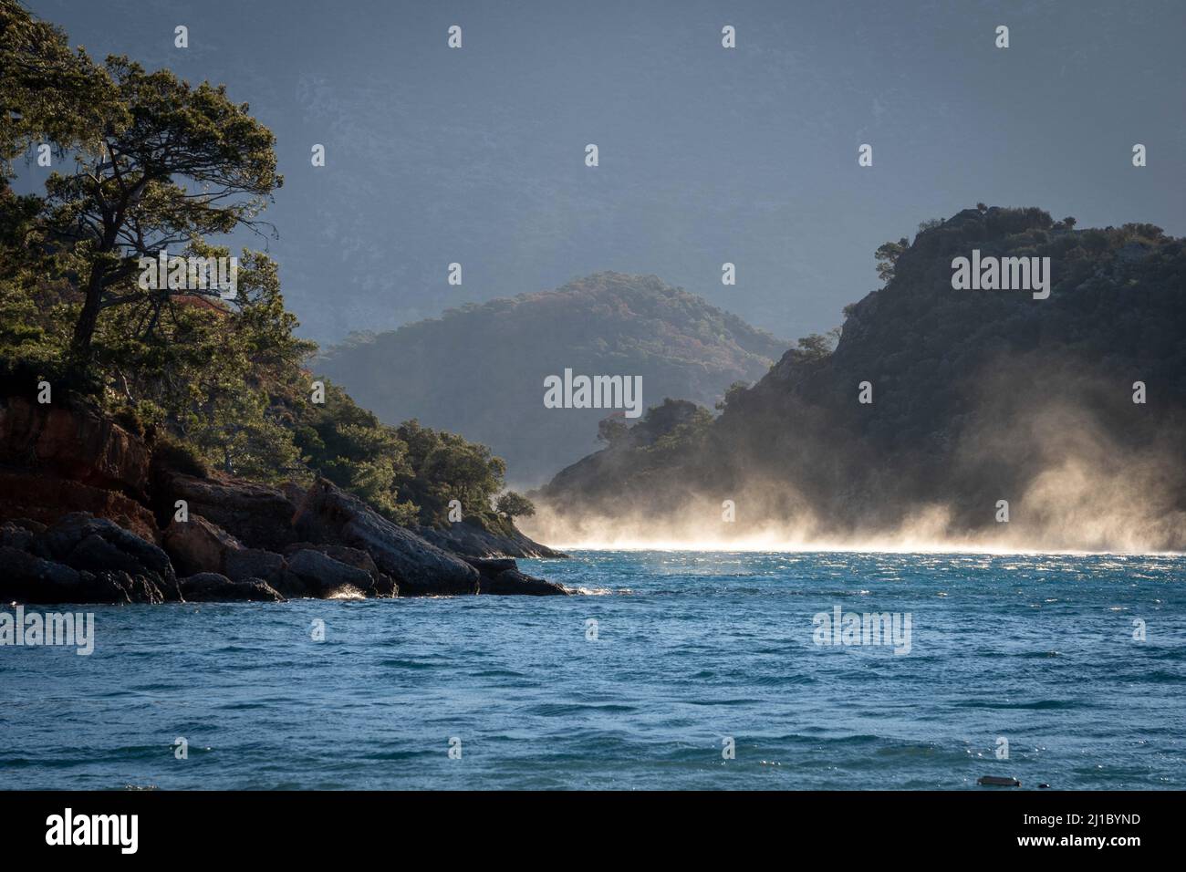 Whirlwinds over the water as the sun rises over the tree covered coast, Turkey Stock Photo