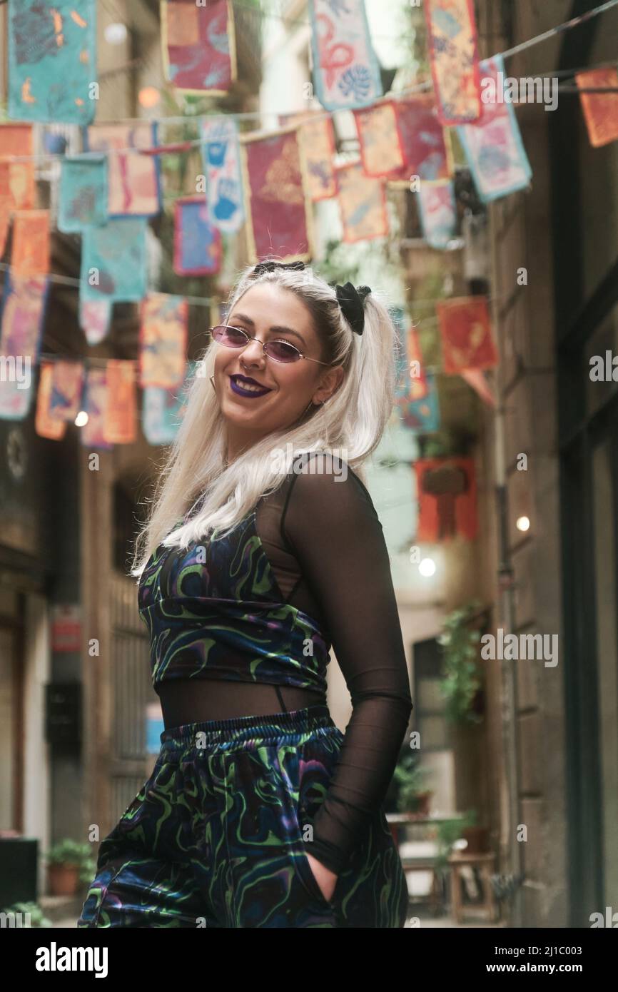 Alternative young woman looking at camera and smiling while posing outdoors on the street. Stock Photo