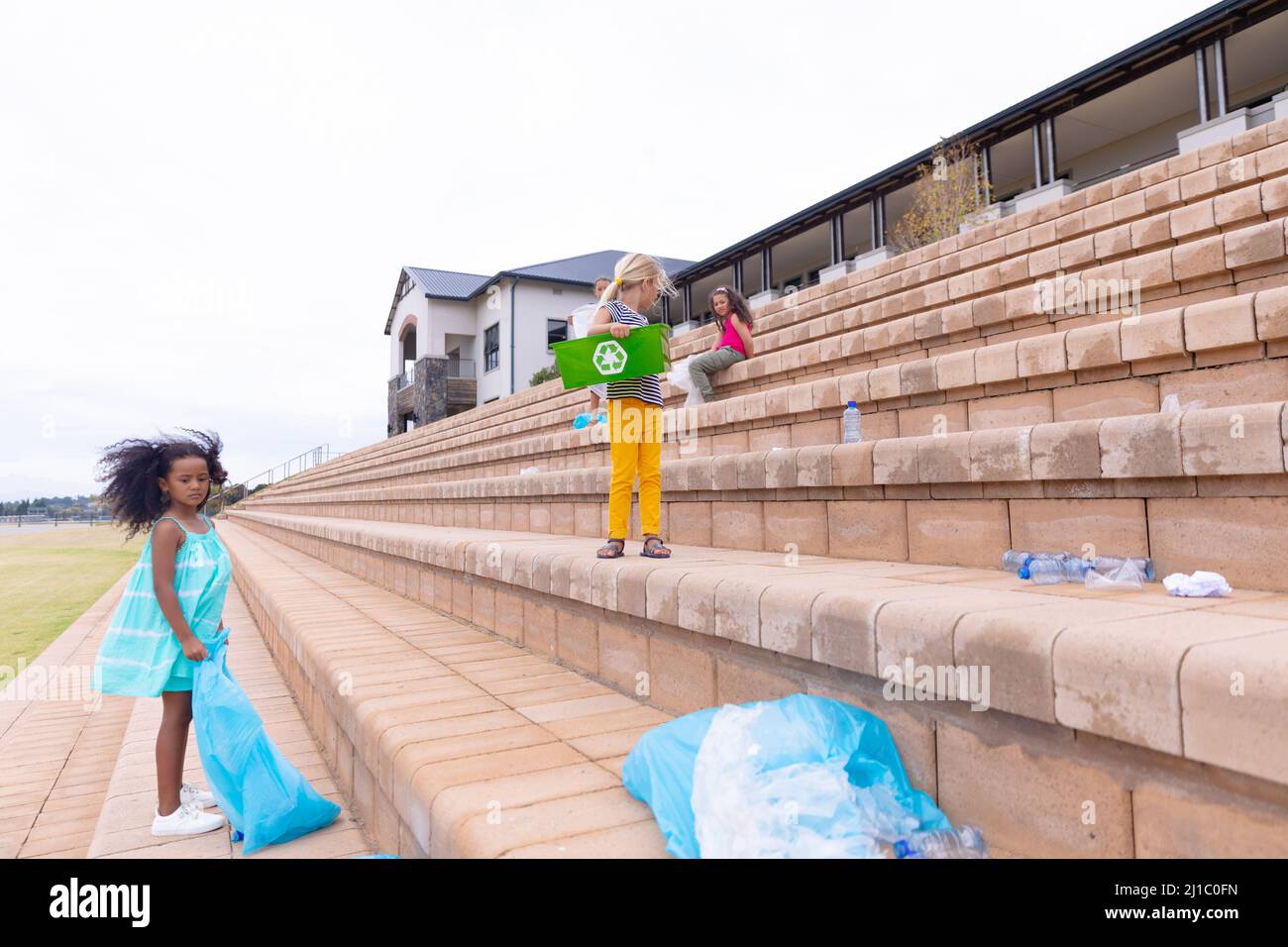 Multiracial elementary schoolgirls collecting plastic in garbage bags while standing on steps Stock Photo