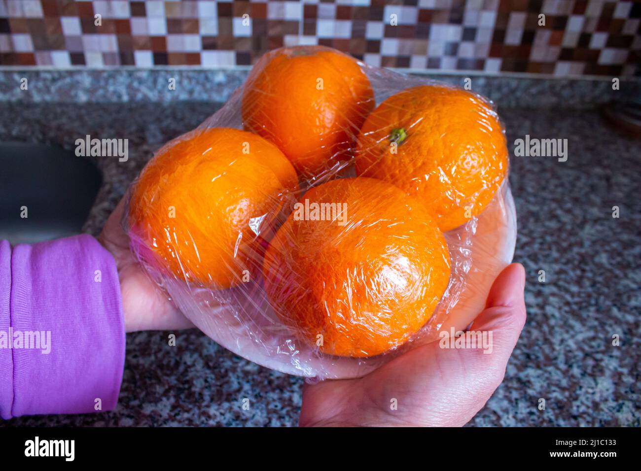 Woman is holding packaged orange fruits in hand. Using food film for fruits storage in fridge. Food storage concept. Stock Photo