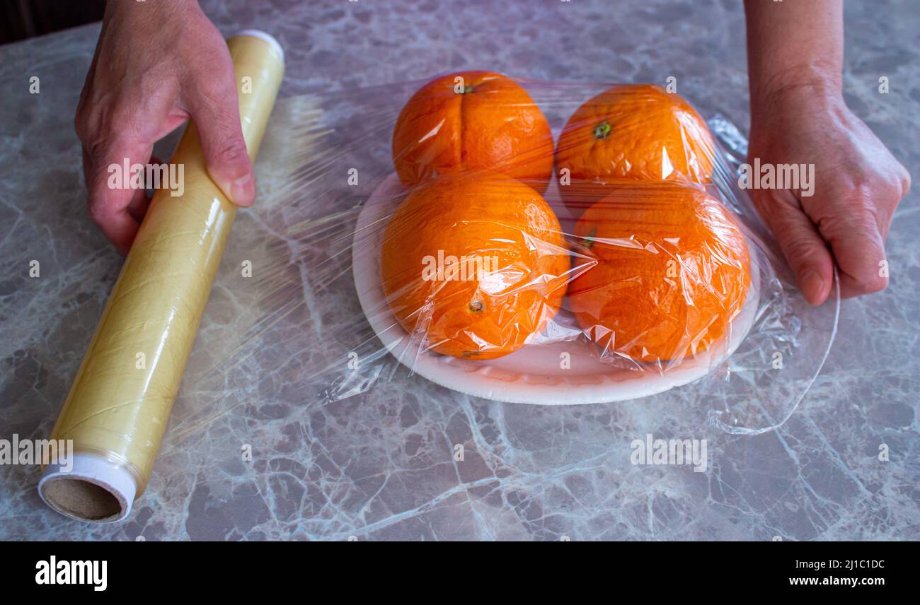 Woman is holding packaged orange fruits in hand. Using food film for fruits storage in fridge. Food storage concept. Stock Photo
