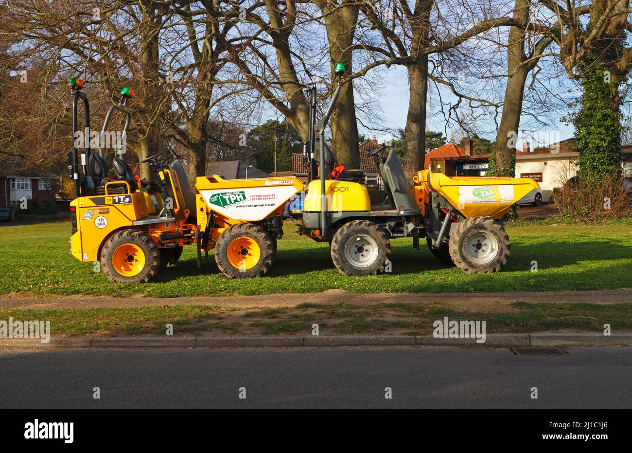 A pair of yellow dumper trucks parked off-road on a small green in a residential area in the Borough of Hellesdon, Norfolk, England, United Kingdom. Stock Photo