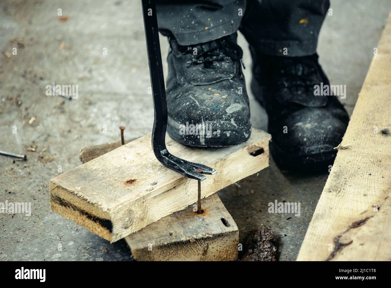 Worker in rough boots pulls nails out of wooden planks. Construction and repair. Background. Stock Photo