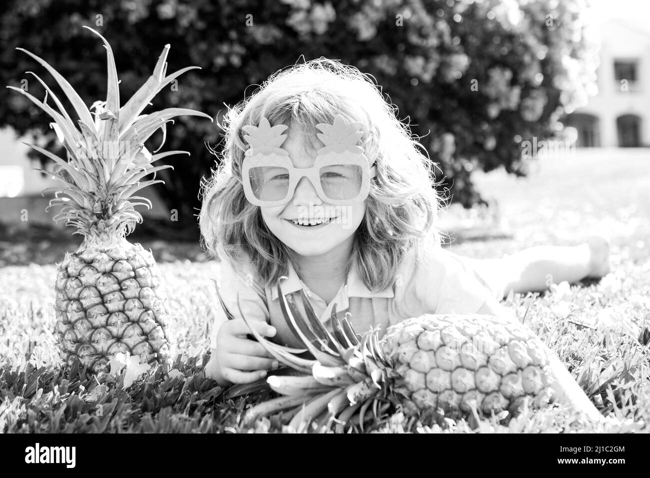 Child wearing funny sunglasses with pineapple. Kid with tropical fruit. Exotic vacation. Fruit for children. Summer kids holiday. Stock Photo