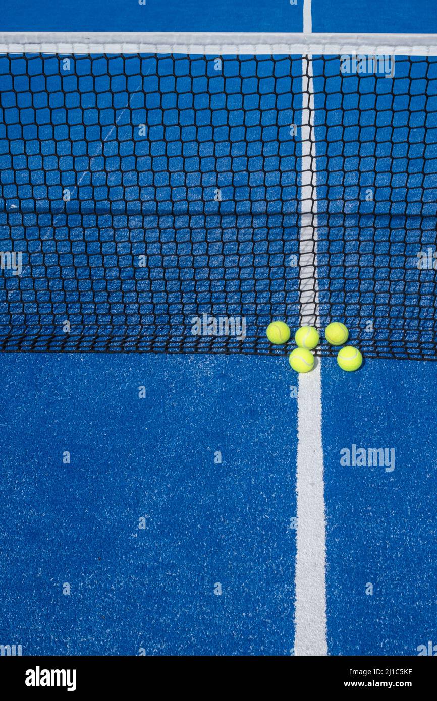 Five tennis balls next to a net of a blue paddle tennis court Stock Photo Alamy