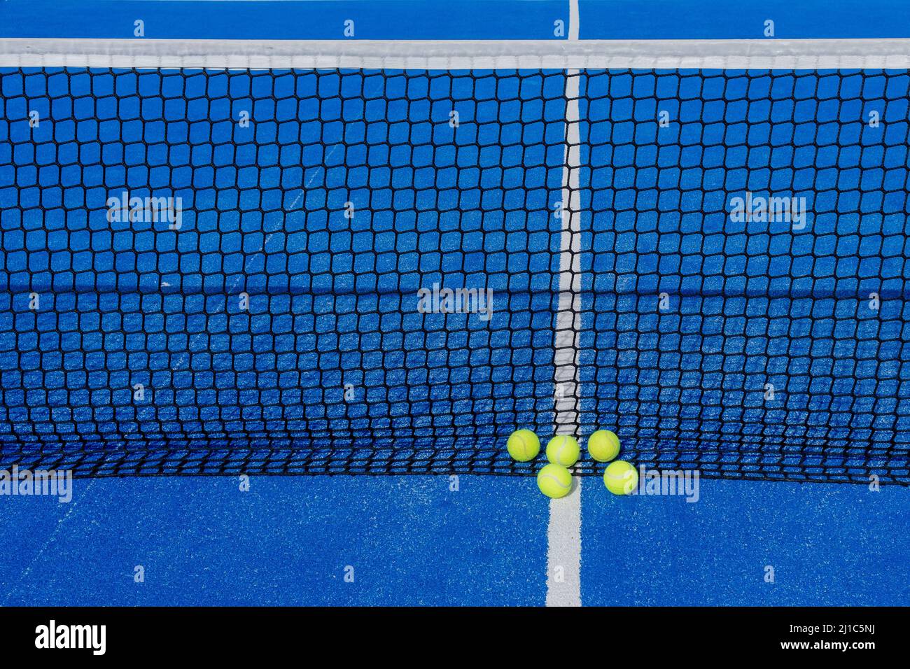 Five tennis balls next to a net of a blue paddle tennis court Stock