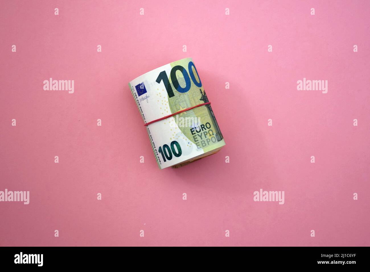 Roll of euro banknotes. 100 euro with red rubber band on pink background. Business, finance, currency Stock Photo