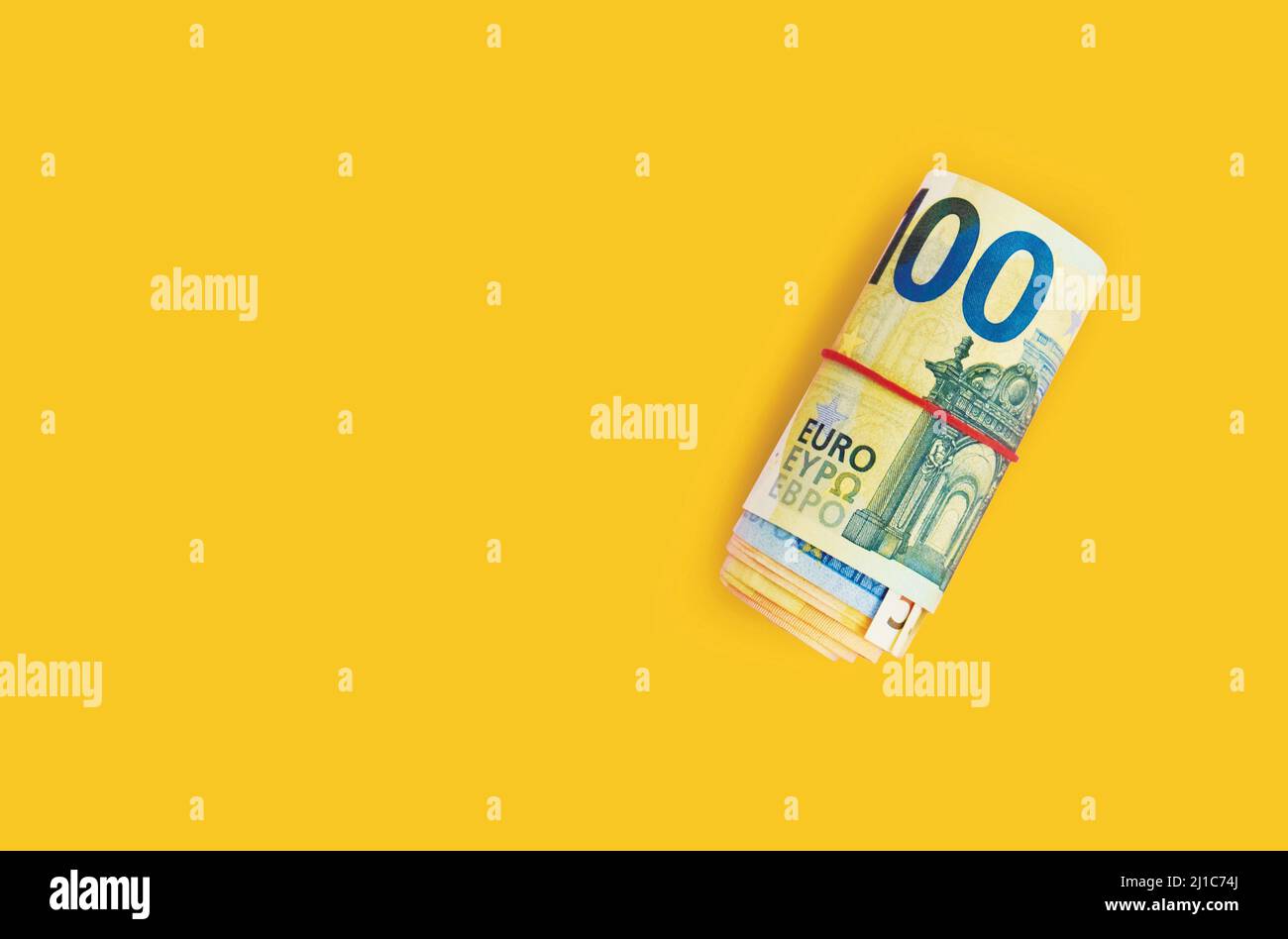 Roll of euro banknotes. 100 euro with red rubber band on yellow background. Business, finance Stock Photo