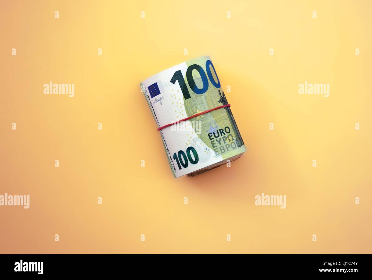 Roll of euro banknotes. 100 euro with red rubber band on yellow background Stock Photo