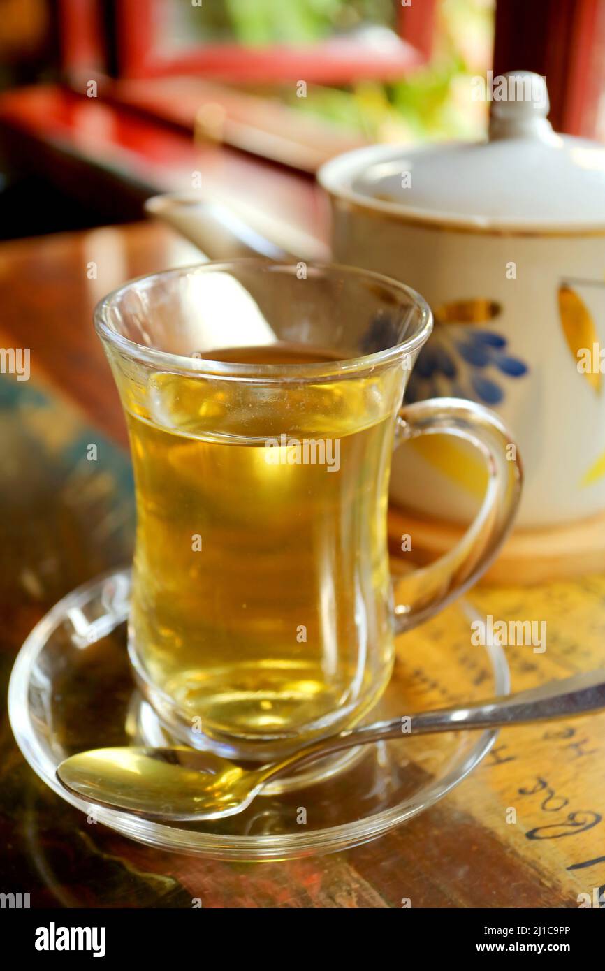 Cup of hot herbal tea in transparent cup with a teapot in the backdrop ...