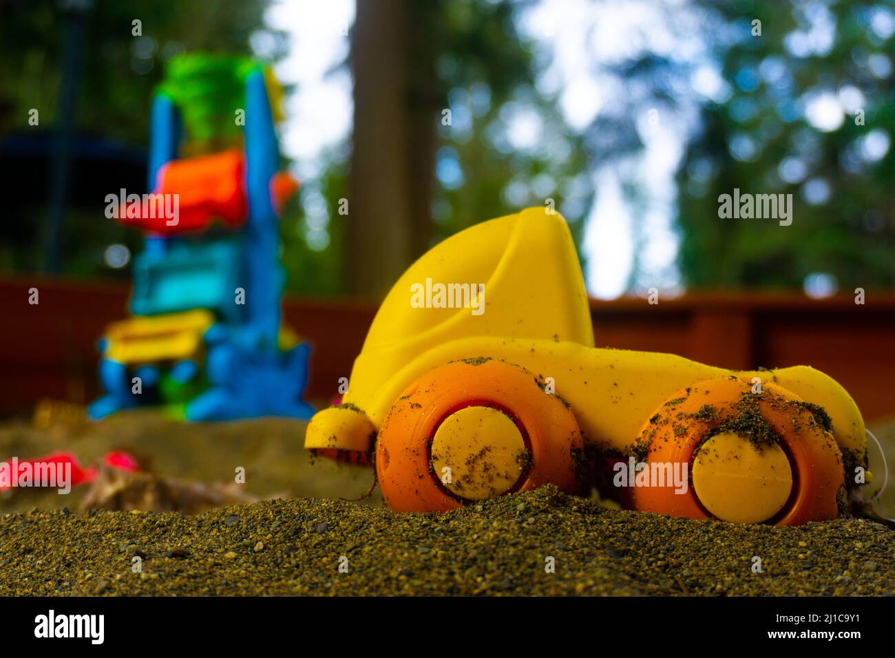 A little truck toy sits in a sand box with other toys blurred out in the background. Stock Photo