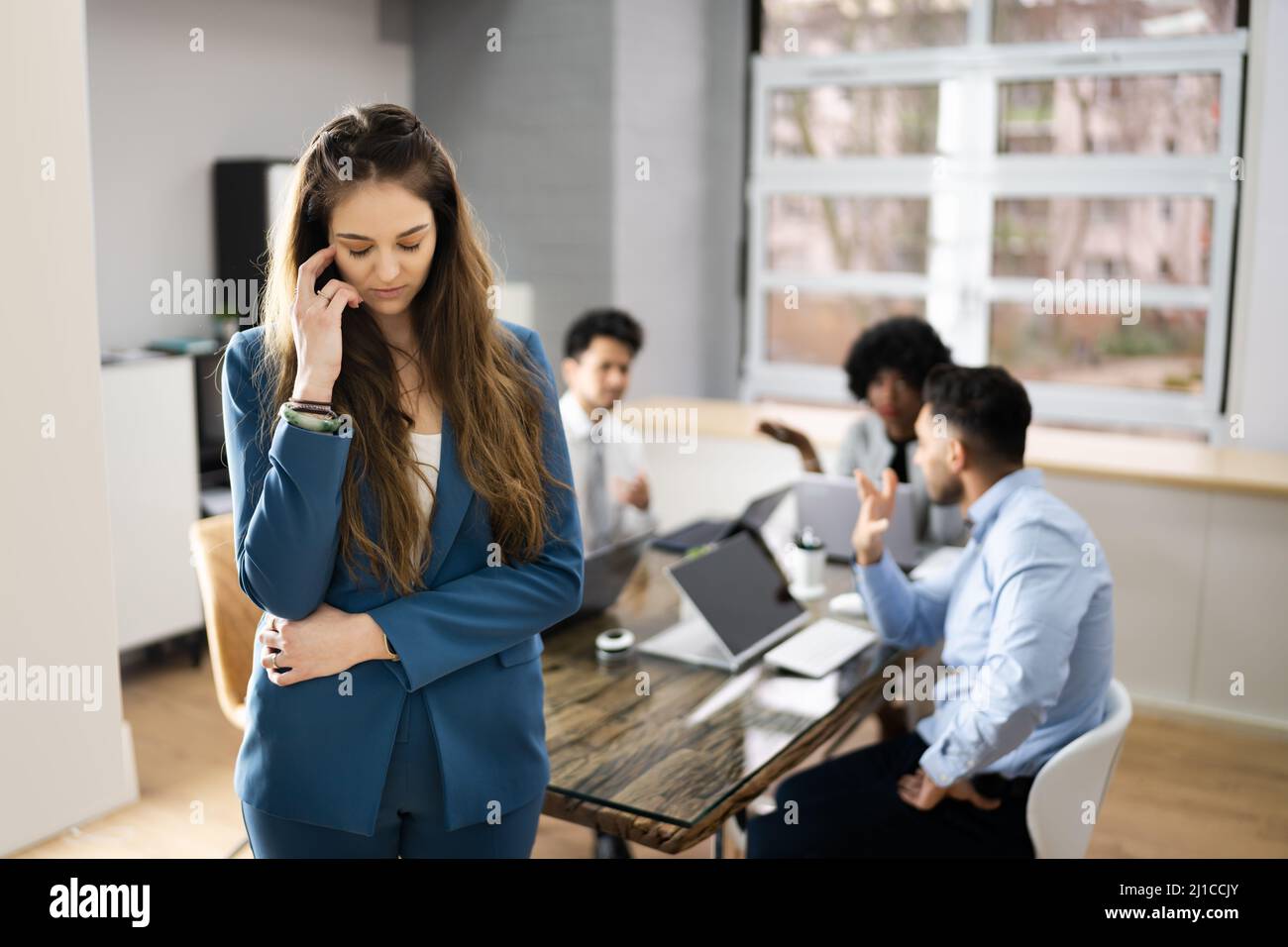 Stressed Female Colleague And Other Workers Bullying In Office Stock Photo