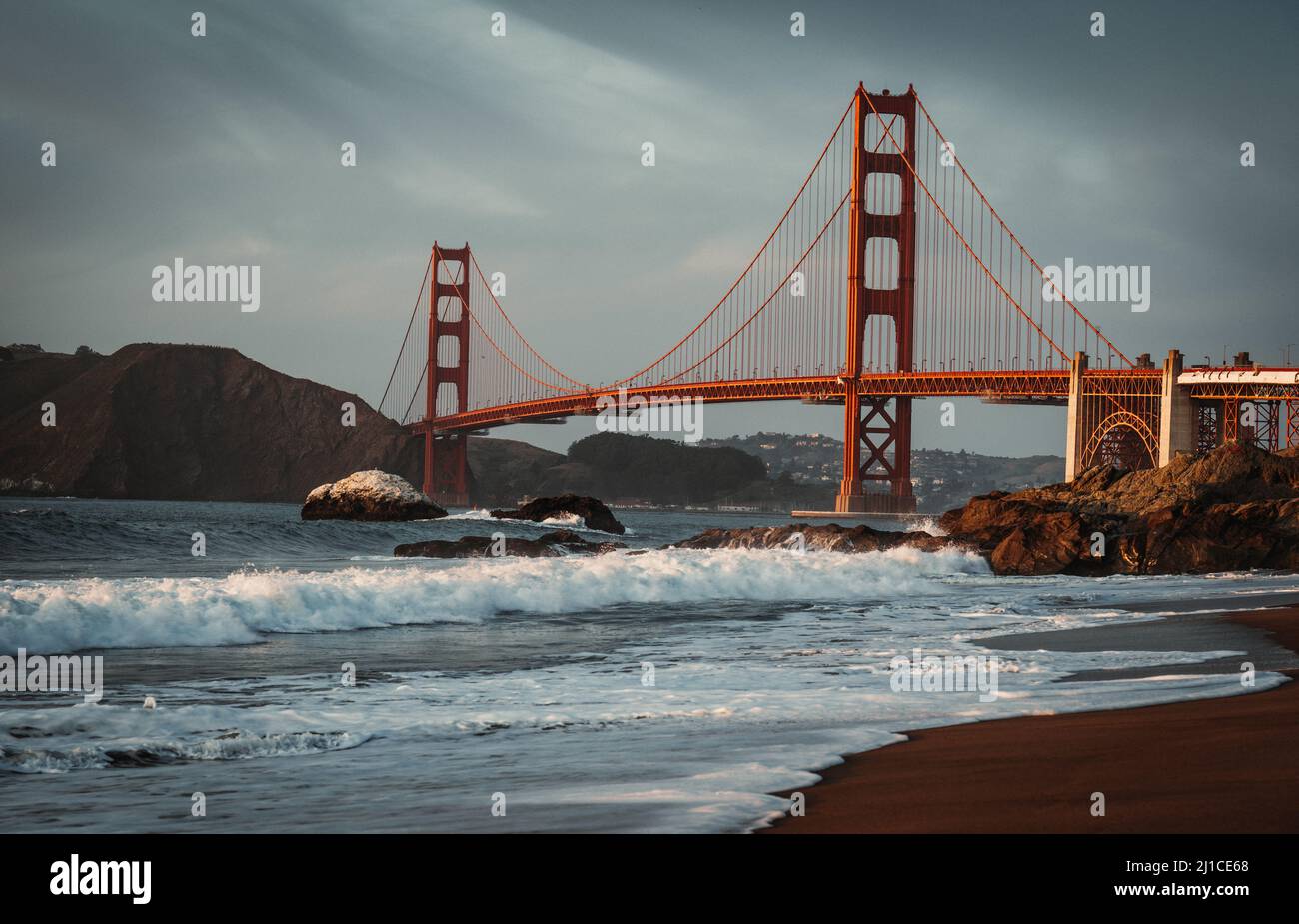A scene with foamy waves rushing to the shore and Golden Gate Bridge in ...