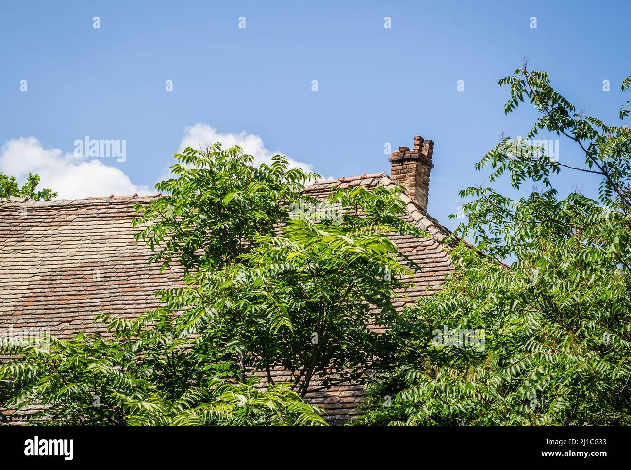 Roofs of houses, covered with old tiles with dilapidated chimneys. Stock Photo