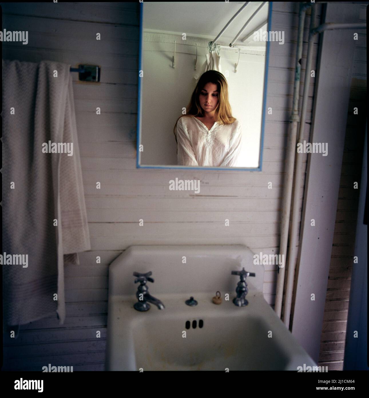 Young woman's reflection in bathroom cabinet mirror, head lowered, looking down Stock Photo