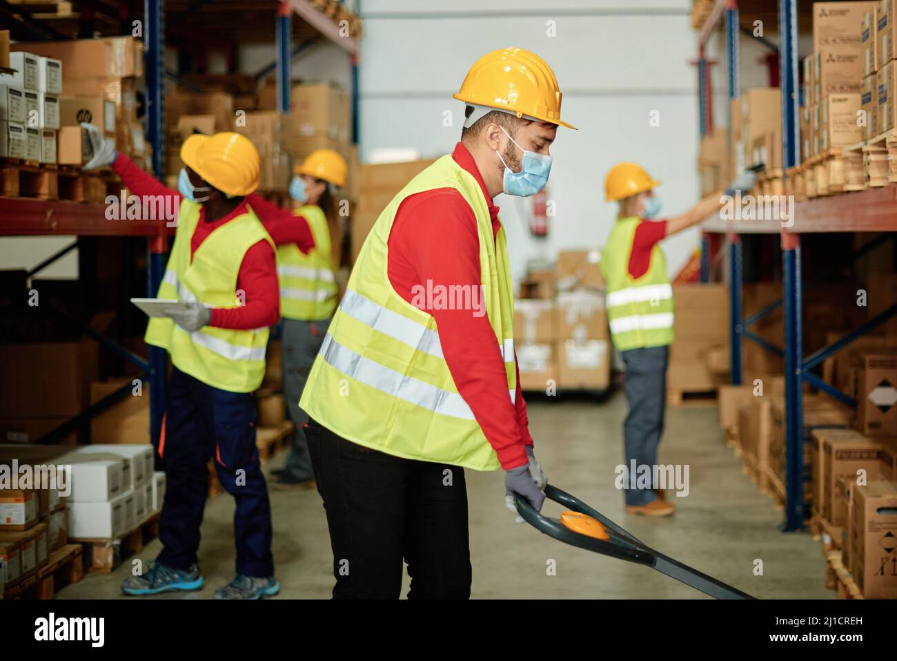 Caucasian adult warehouse worker works loading boxes of goods while wearing a safety mask - Focus on the face Stock Photo