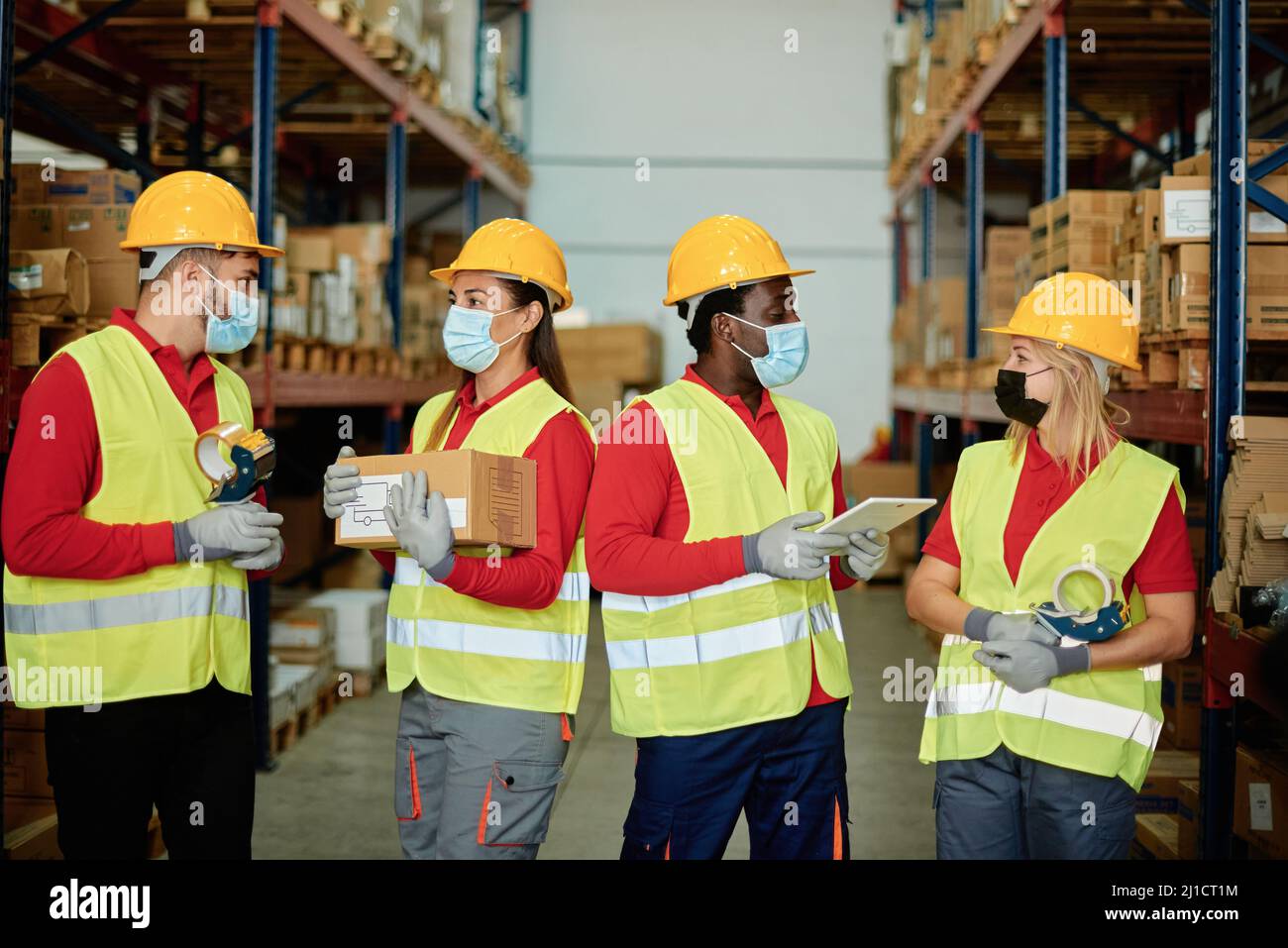Multiracial group of warehouse workers hold delivery box, order ipad while wearing safety mask for coronavirus prevention - Focus on faces Stock Photo
