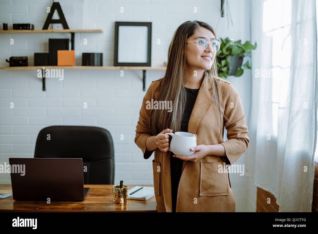Mexican young woman drinks from a white cup with natural pose in her home office Stock Photo