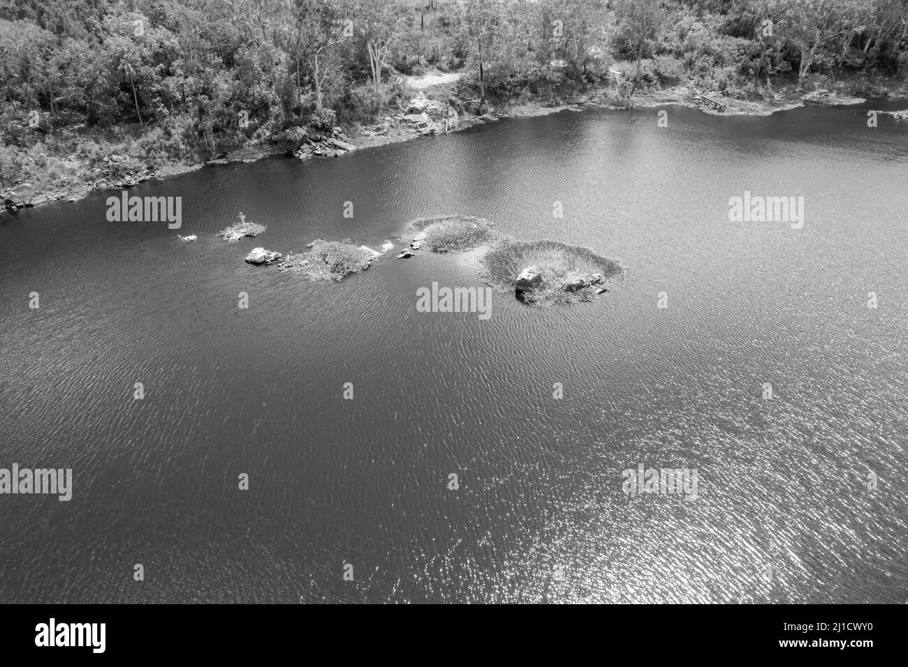 Rocks in the middle of a dammed river covered in green vegetation. Dumbleton Weir, Mackay, Queensland, Australia. Monotone image. Stock Photo