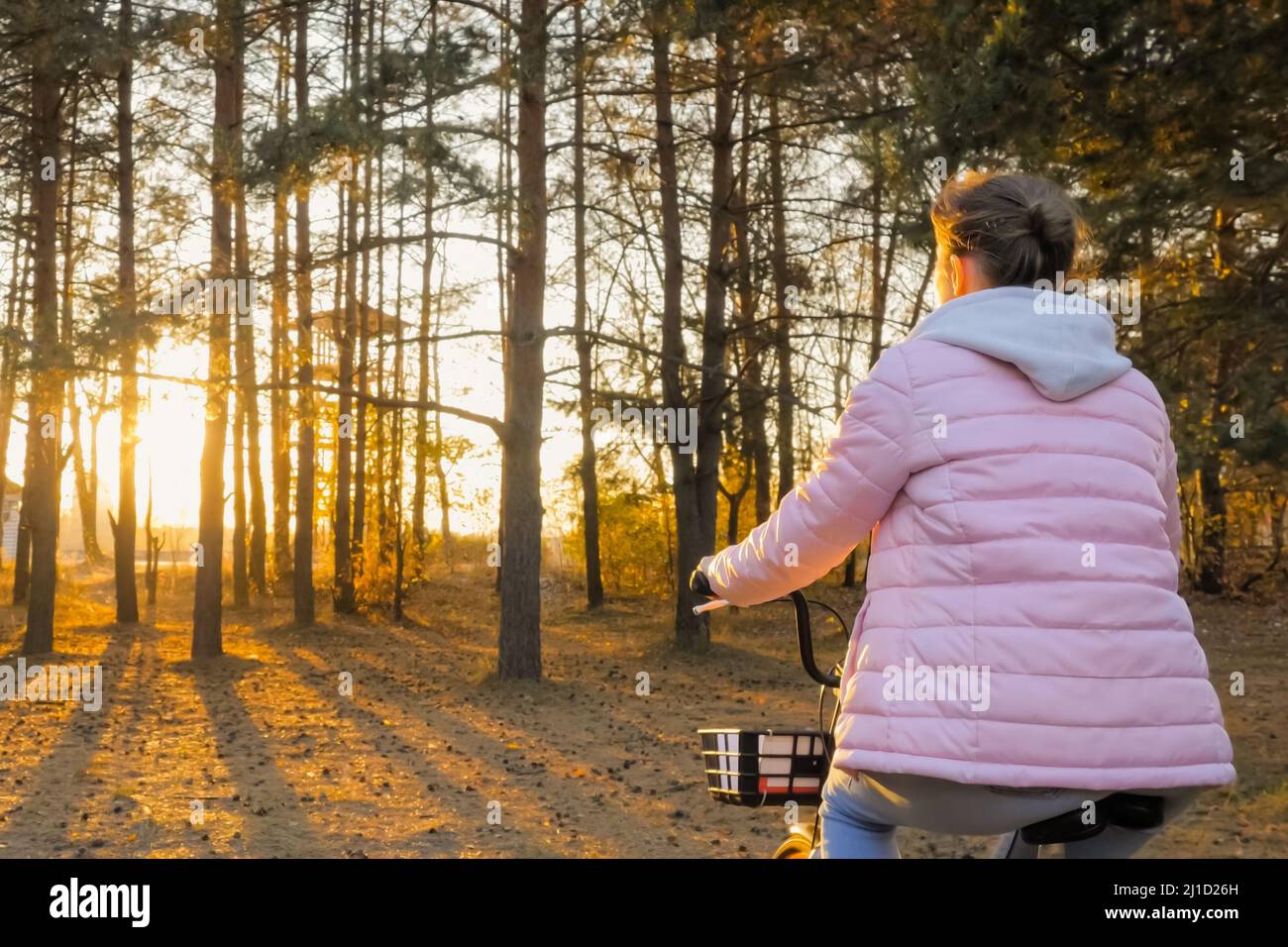 Young woman riding bicycle in autumn city park at sunset with sun lens flares Stock Photo