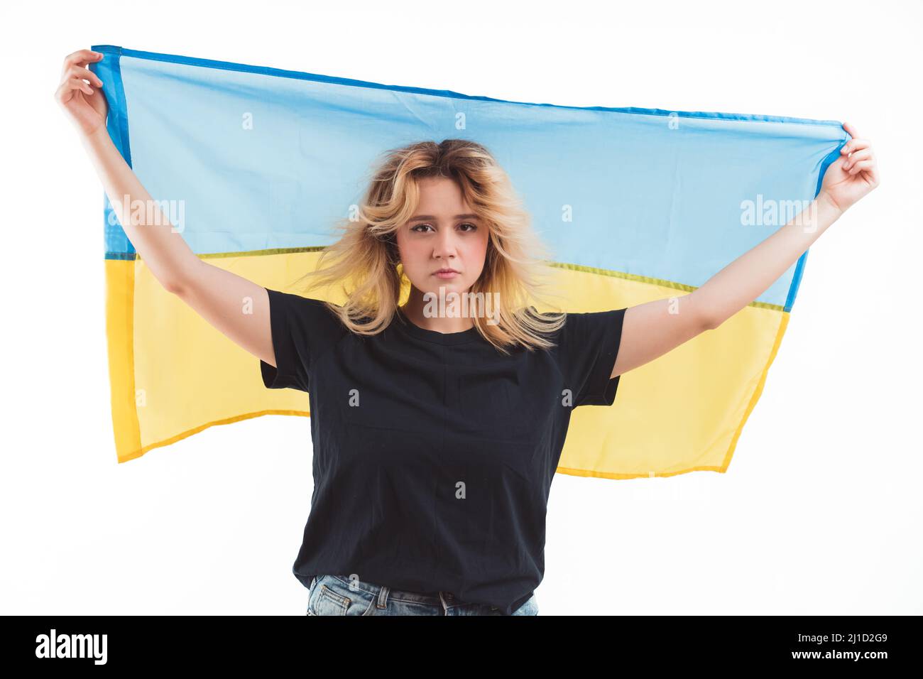 Sad caucasian young woman holding up Ukrainian flag. Support for Ukraine. No more war. Isolated over white background. High quality photo Stock Photo