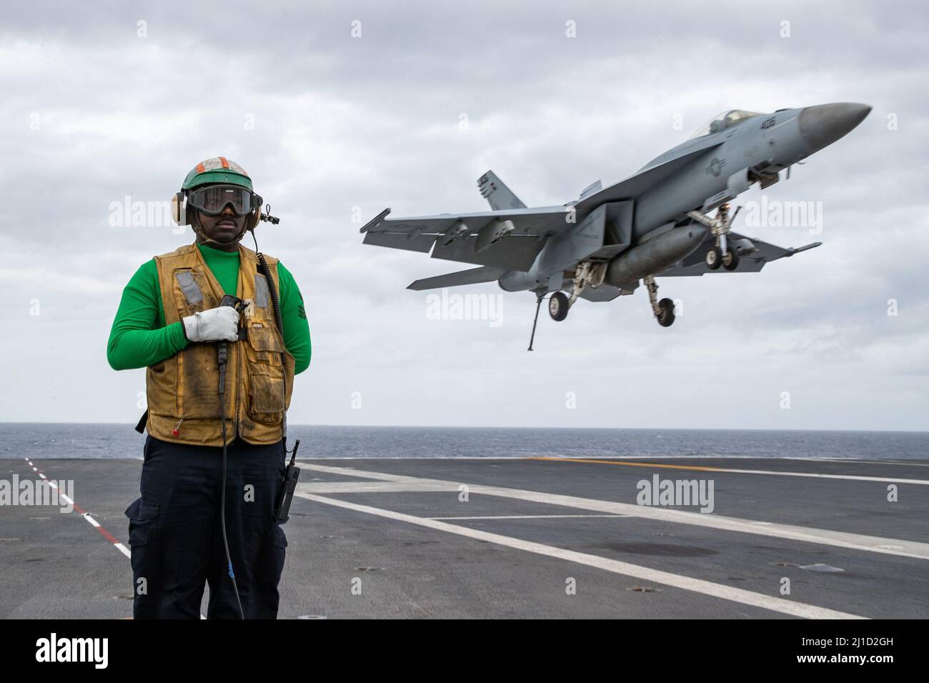 Aviation Boatswain's Mate (Equipment) 1st Class Gabriel Cooper, from Stone Mountain, Georgia, assigned to USS Gerald R. Ford's (CVN 78) air department, stands watch as the arresting gear officer as an F/A-18E Super Hornet attached to the 'Golden Warriors' of Strike Fighter Squadron (VFA) 87 approaches the flight deck for landing during flight operations, March 23, 2022. Ford is underway in the Atlantic Ocean conducting flight deck certification and air wing carrier qualifications as part of the ship’s tailored basic phase prior operational deployment. (U.S. Navy photo by Mass Communication Spe Stock Photo
