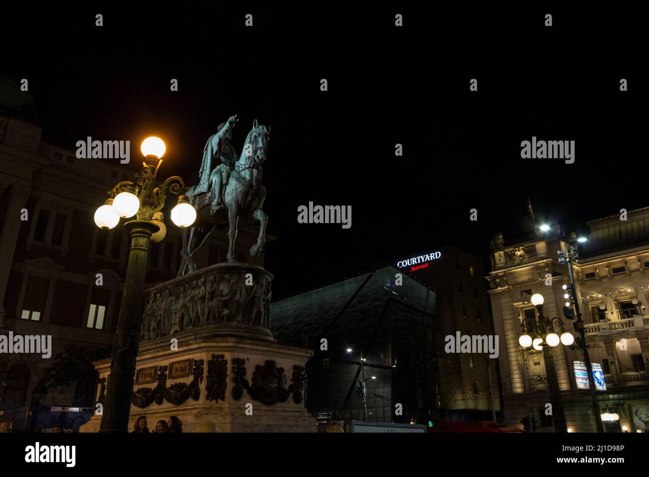 Picture of the statue of Prince Mihailo in front, on Trg Republike, also called republic square at noght with people passing by. Republic Square or Sq Stock Photo