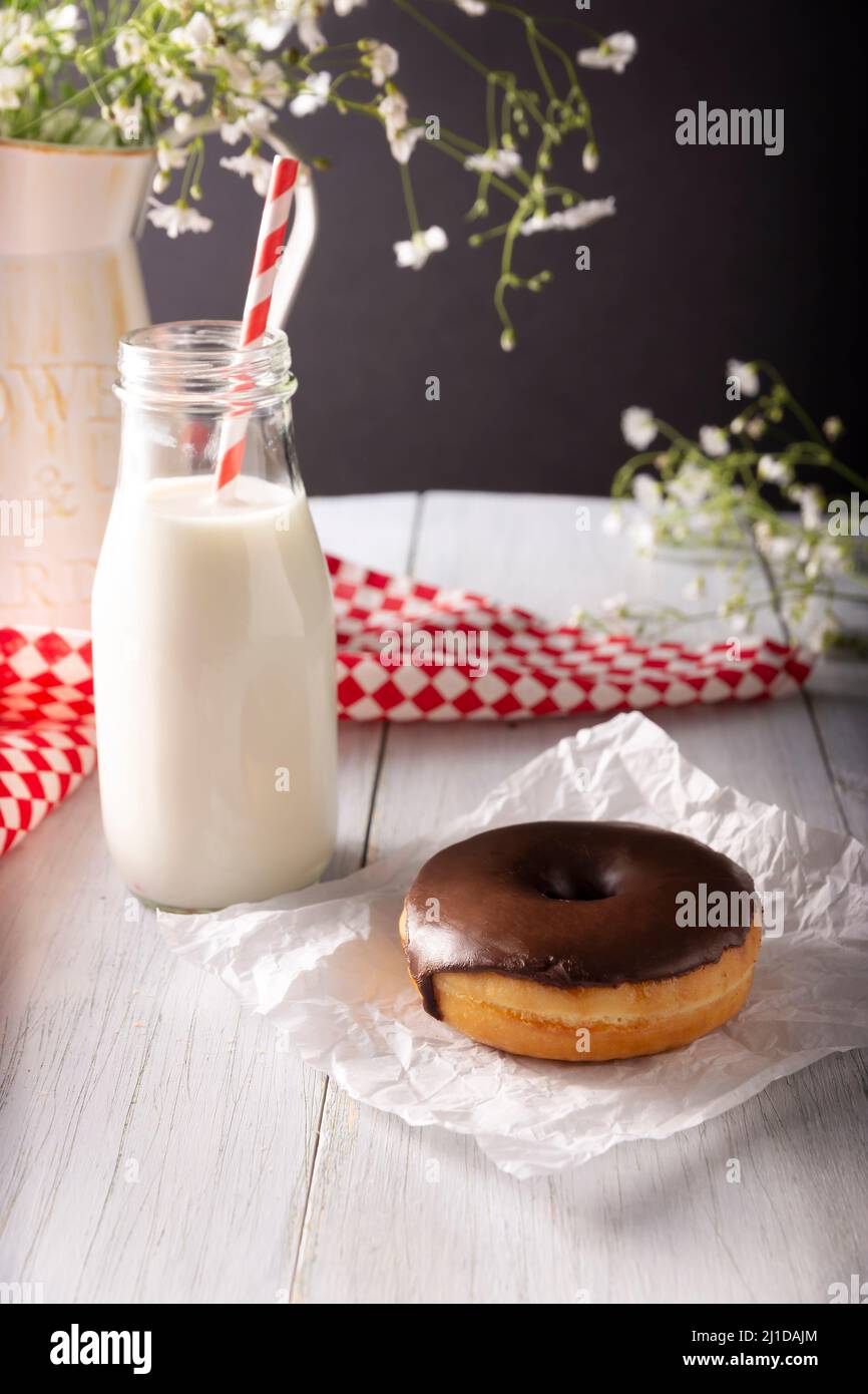 Homemade donut covered with chocolate glaze and glass of milk on white rustic wooden surface Stock Photo