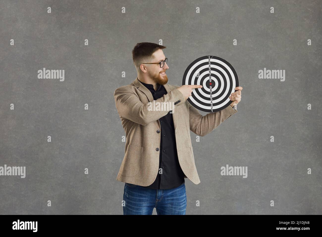 Happy young businessman holding a shooting target and pointing right at the bullseye Stock Photo