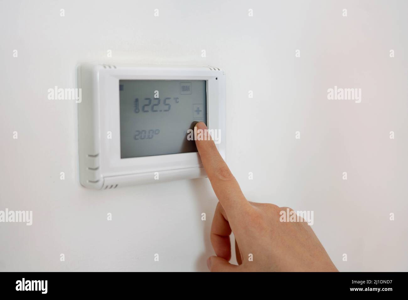 Lowering the temperature for energy saving. Human hand adjusting digital central heating thermostat at home. Stock Photo