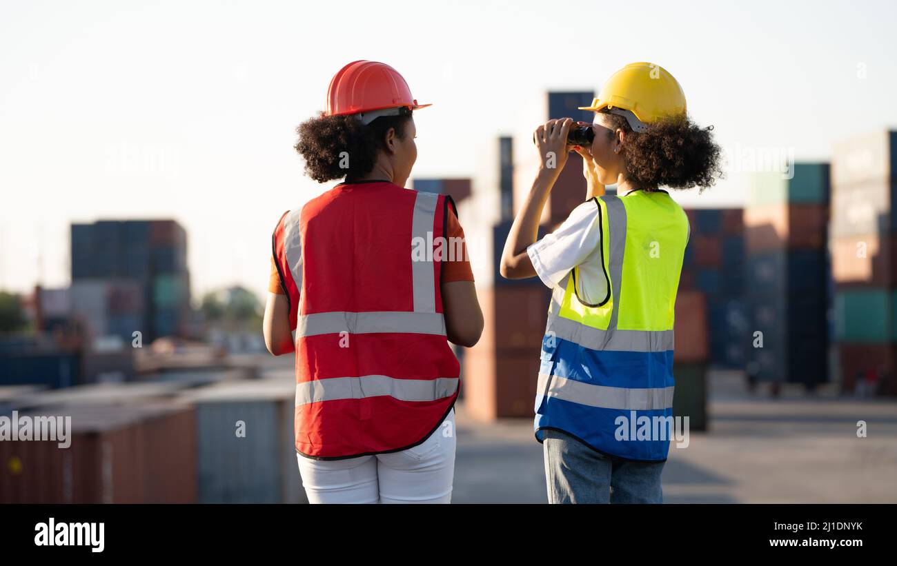 Woman foreman or engineer using binoculars and partner pointing at problem focus cargo container tank at the warehouse container logistic transportati Stock Photo