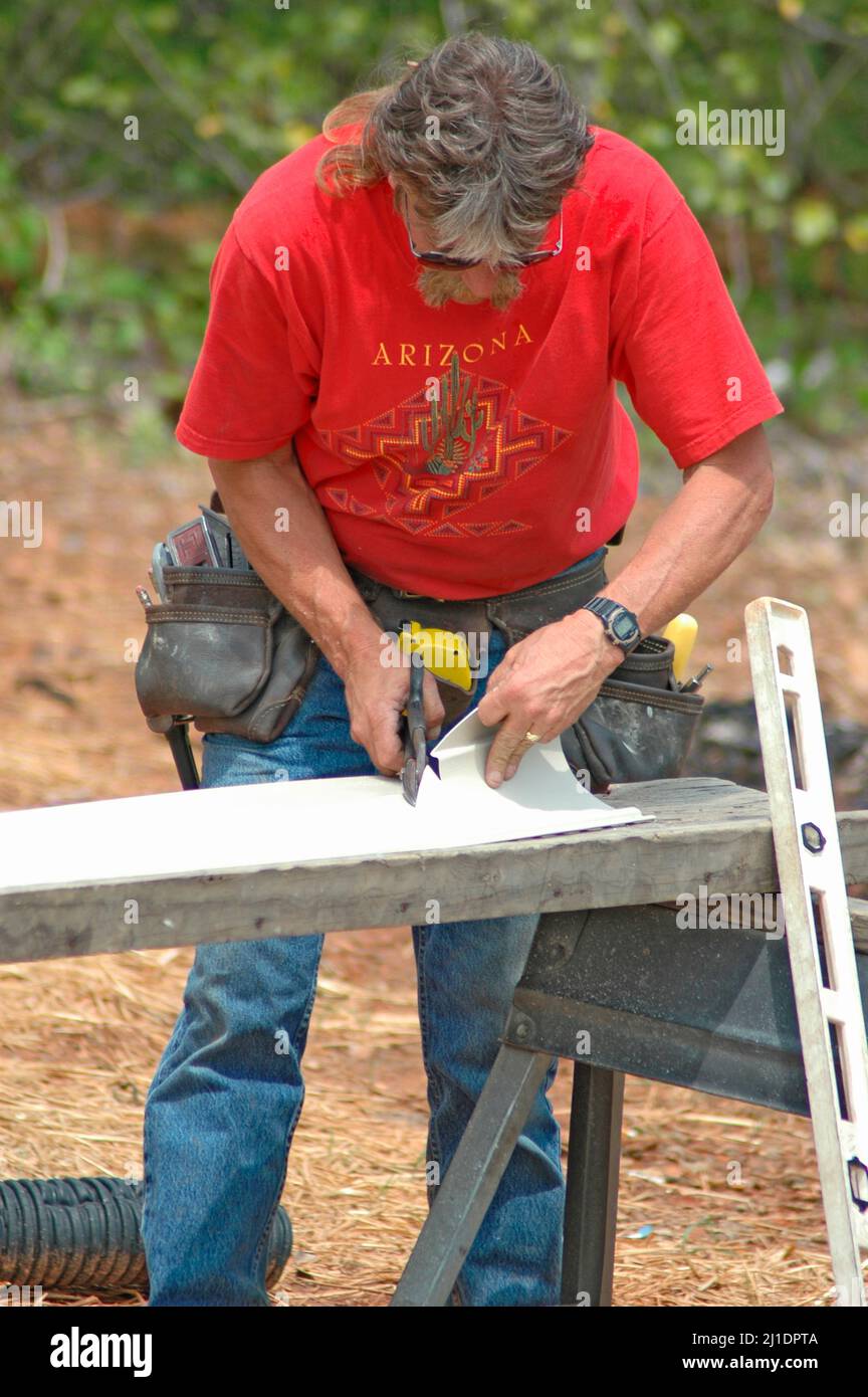 Installing vinyl siding on new home construction on ladder and using nail gun and chop saw and