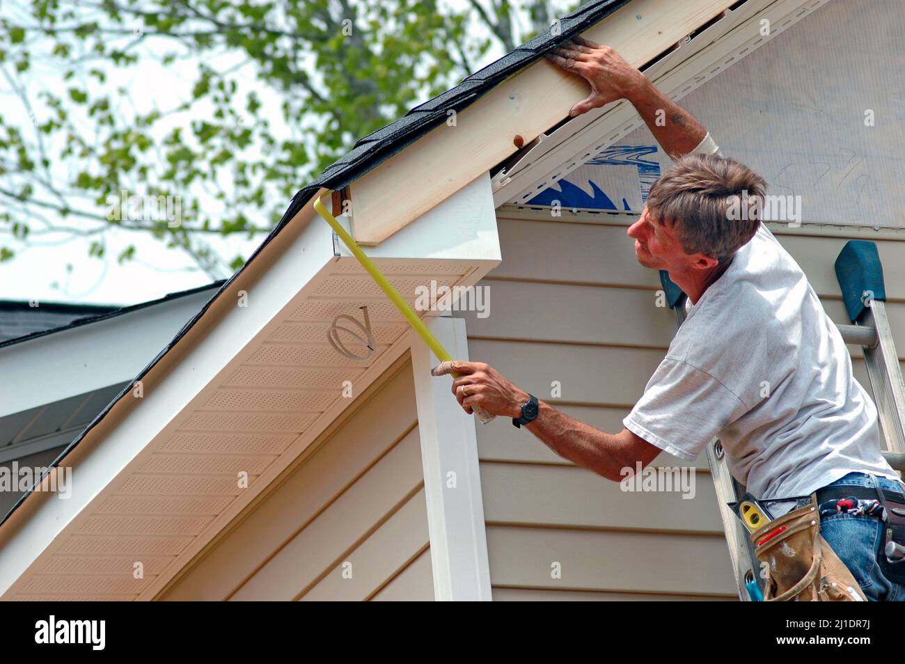 Installing vinyl siding on new home construction on ladder and using