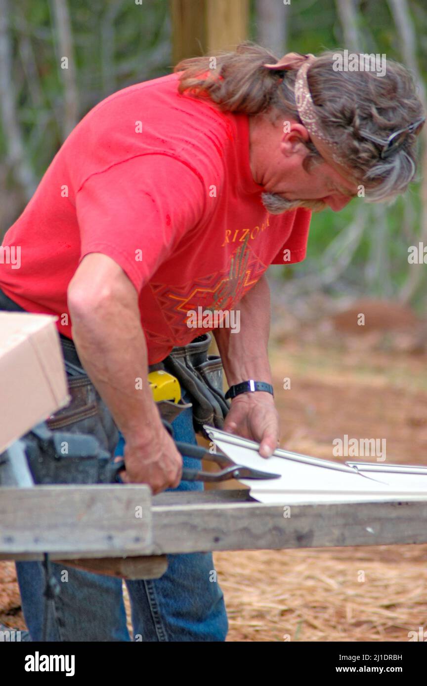 Installing vinyl siding on new home construction on ladder and using nail gun and chop saw and