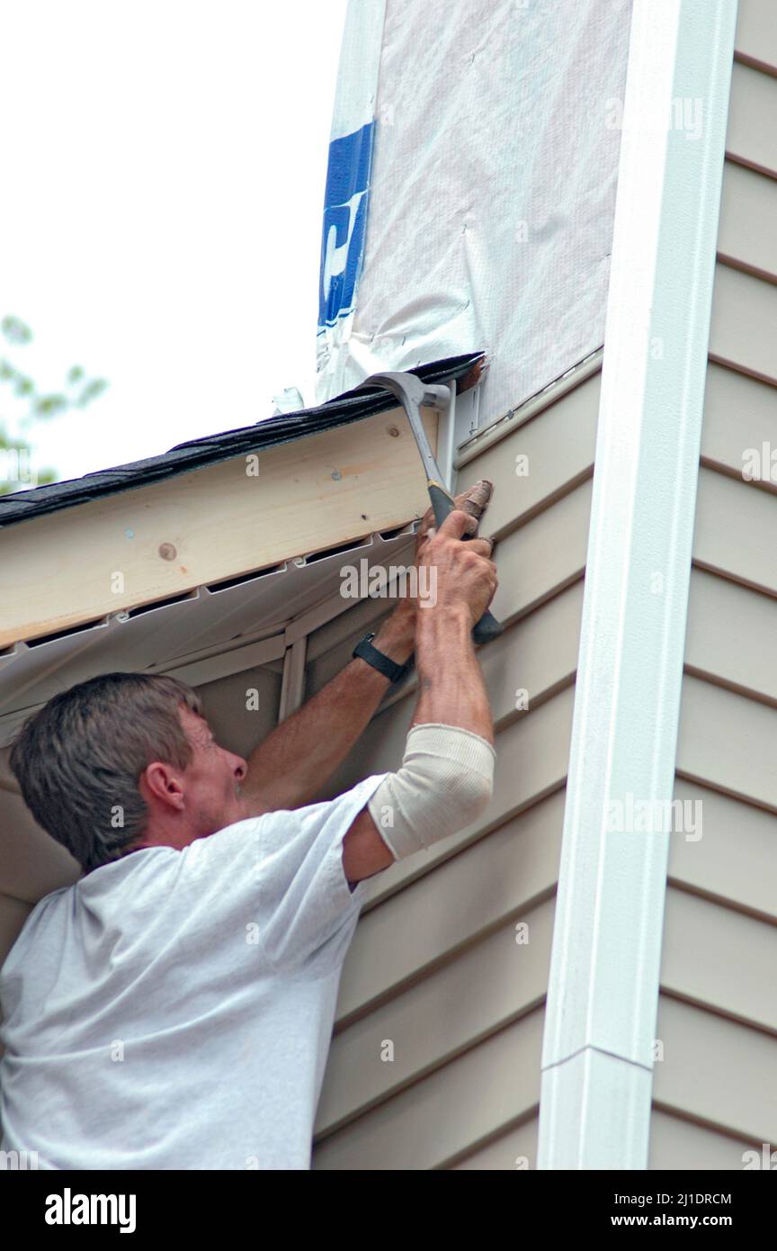 Installing vinyl siding on new home construction on ladder and using nail gun and chop saw and