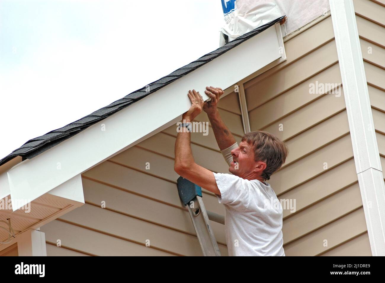 Installing vinyl siding on new home construction on ladder and using
