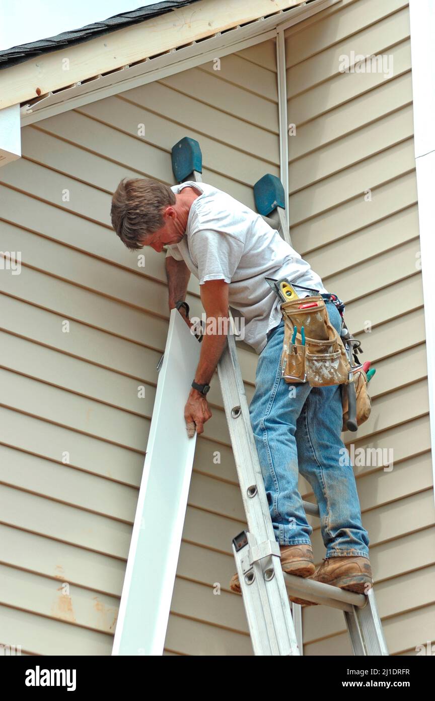 Installing vinyl siding on new home construction on ladder and using