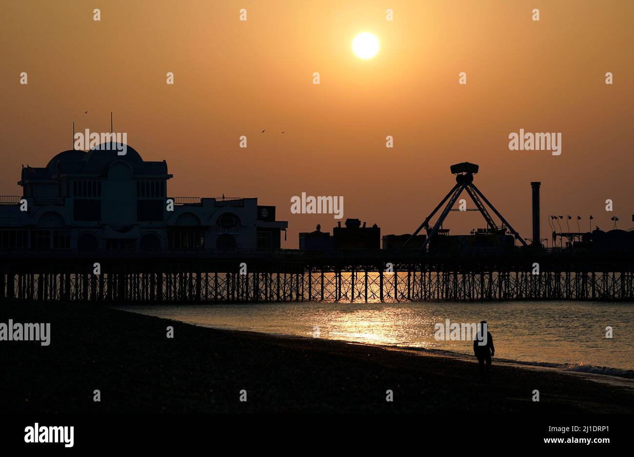 A person walks along the beach as the sun rises above South Parade pier in Southsea, Hampshire. Picture date: Friday March 25, 2022. Stock Photo