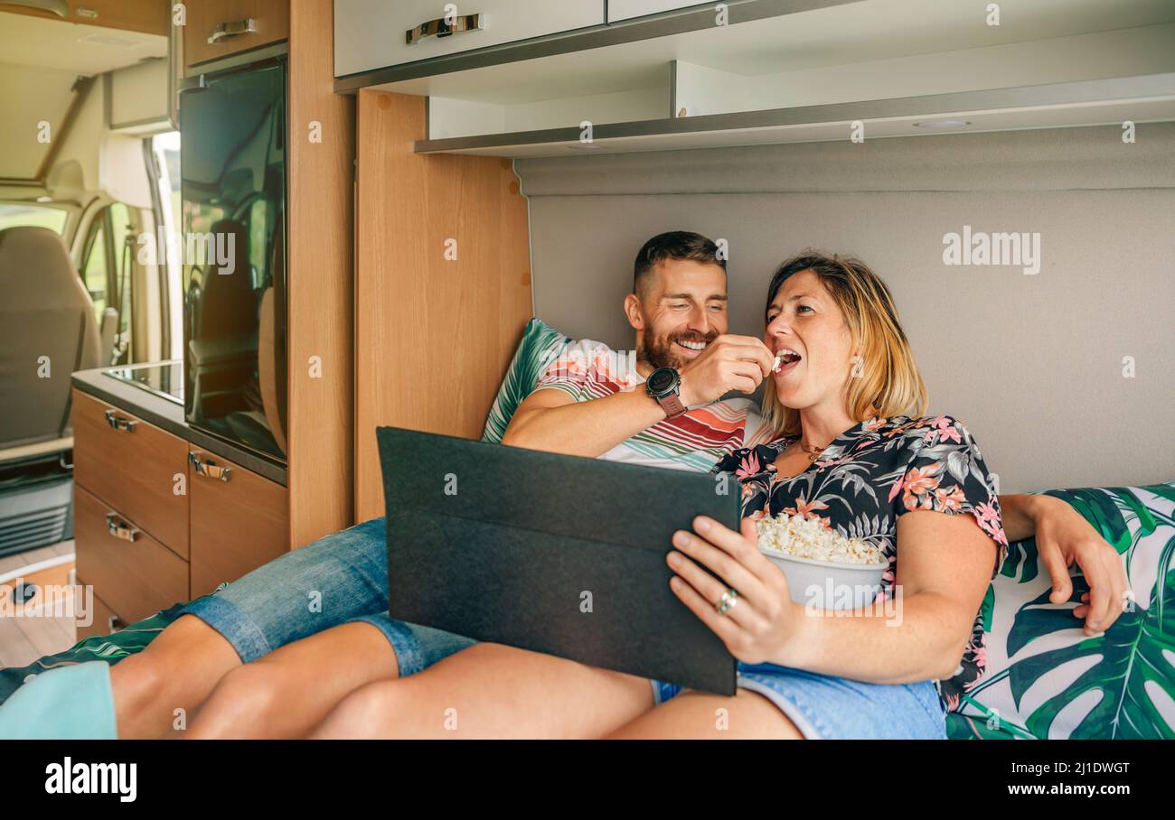 Man feeding his girlfriend a popcorn watching a movie on the tablet in their camper van Stock Photo