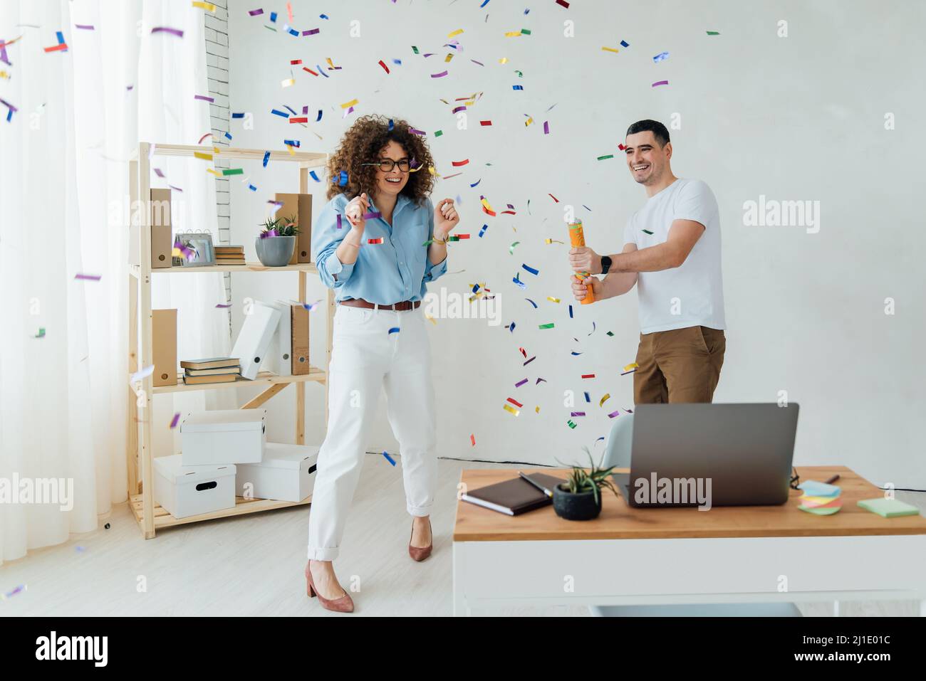 Two colleagues celebrating birthday or starting new business in office. Confetti in the air Stock Photo