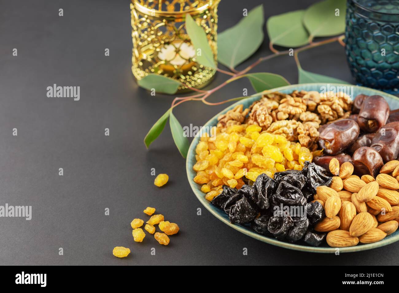 Ramadan concept. Nuts, dried fruits and dates in the blue bowl, glass of water and ramadan lantern on a black background with copy space. Arab dish, s Stock Photo